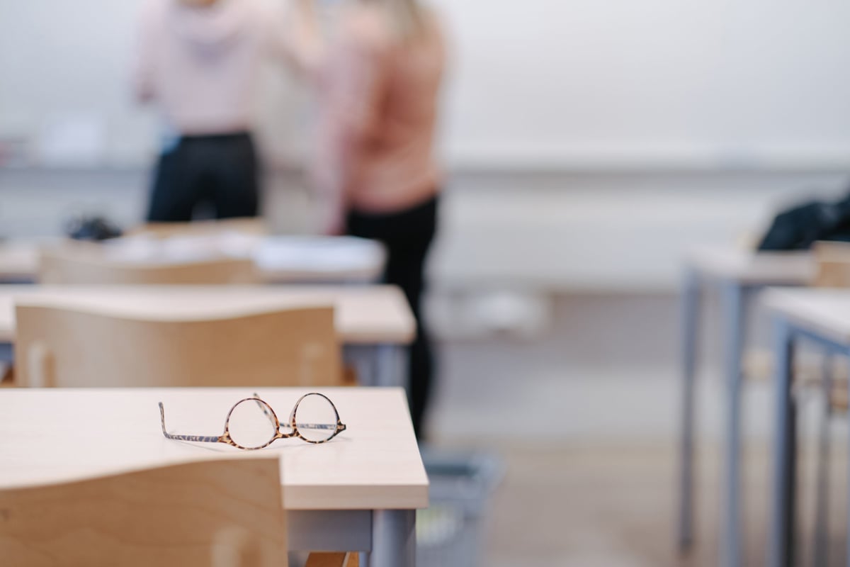 Glasses resting on a wooden desk in a classroom